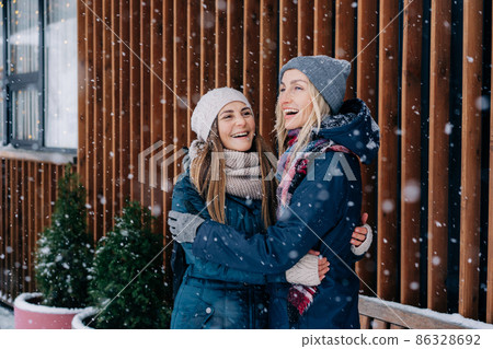 Adult female friends embracing and laughing rejoicing at the meet and snowy cold weather. 86328692