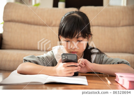 Elementary school girl looking at a smartphone while studying 86328694