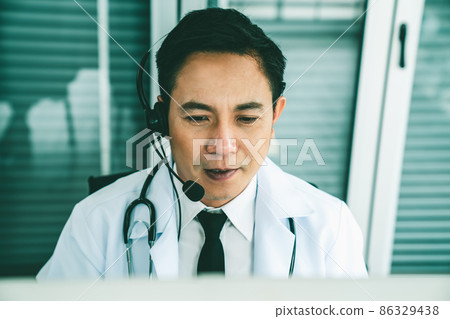 Doctor wearing headset talking actively on video call in a clinic or hospital . Doctor wearing headset talking actively on video call in a clinic or hospital . 86329438