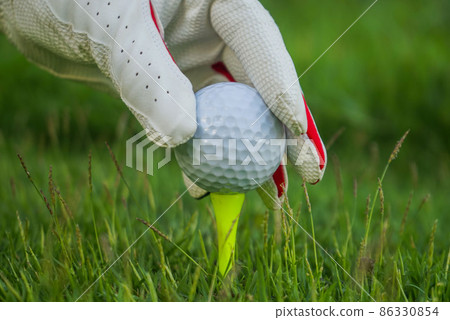 Hand ware leather glove putting golf ball on tee off in course Hand ware leather glove putting golf ball on tee off in course 86330854