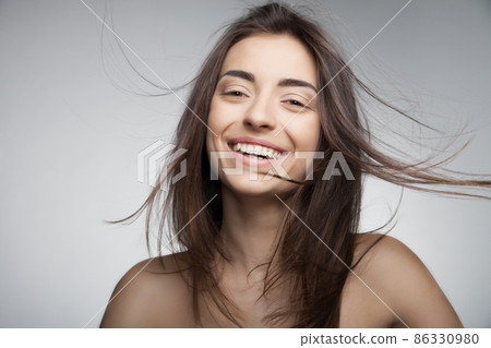 Attractive smiling woman with long hair on grey Attractive smiling woman with long hair on grey 86330980