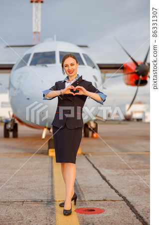 Cheerful flight attendant showing heart sign at airport Cheerful flight attendant showing heart sign at airport 86331307