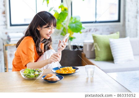 A young woman looking at her smartphone while eating at the dining room 86335052