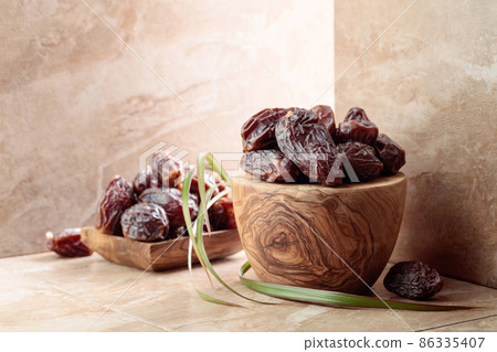 Dates fruit in a wooden bowl on a beige ceramic table. 86335407