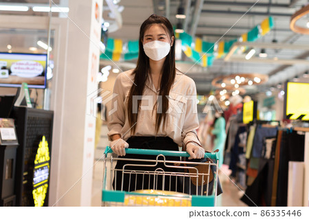 Beautiful attractive asian woman wearing medical face mask and rubber gloves for protected virus and bacteria smile with shopping cart in supermarket happiness and enjoy,Shopping in Grocery Concept 86335446