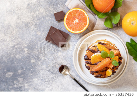 Celebrating Pancake day, healthy breakfast. Delicious homemade american bananas pancakes with chocolate and red orange on grey stone background. Flat lay, top view. Copy space. 86337436