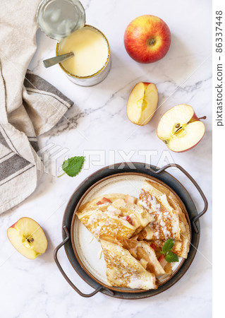 Celebrating Pancake day, healthy breakfast. Homemade sweet crepes with apples and condensed milk on a marble tabletop. Top view flat lay. Celebrating Pancake day, healthy breakfast. Homemade sweet crepes with apples and condensed milk on a marble tabletop. Top view flat lay. 86337448