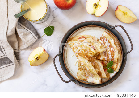 Celebrating Pancake day, healthy breakfast. Homemade sweet crepes with apples and condensed milk on a marble tabletop. Top view flat lay. Celebrating Pancake day, healthy breakfast. Homemade sweet crepes with apples and condensed milk on a marble tabletop. Top view flat lay. 86337449