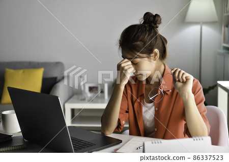Tired young Asian woman with eyes pain during working in home office using laptop. Overworked tired Tired young Asian woman with eyes pain during working in home office using laptop. Overworked tired 86337523