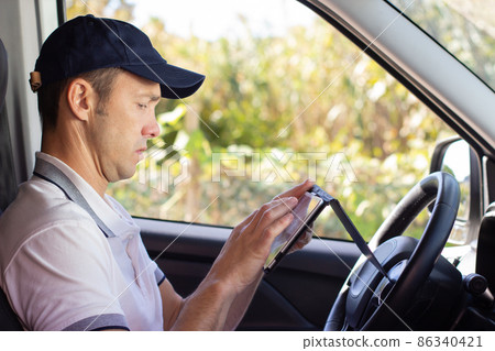 Focused deliveryman checking mobile phone in car Focused deliveryman checking mobile phone in car 86340421