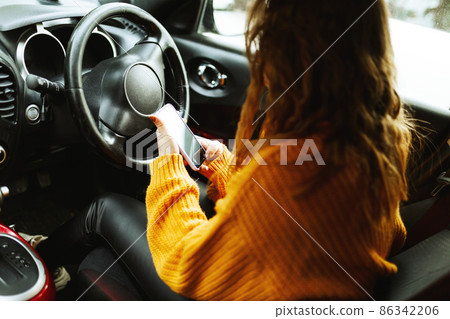 Portrait of a young casual woman in orange sweater, texting on her smartphone or making video call ,while driving or traffic stop a car during lunch break. Portrait of a young casual woman in orange sweater, texting on her smartphone or making video call ,while driving or traffic stop a car during lunch break. 86342206