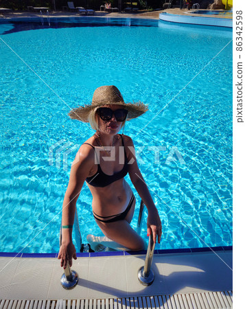 Sexy Woman in Swimsuit is Relaxing in Swimming Pool. Beautiful Woman Wearing Straw Hat and Relax Sunbathe in Poolside on Summer Holiday at Resort Hotel, Leisure Activities and Relaxation Time Sexy Woman in Swimsuit is Relaxing in Swimming Pool. Beautiful Woman Wearing Straw Hat and Relax Sunbathe in Poolside on Summer Holiday at Resort Hotel, Leisure Activities and Relaxation Time 86342598