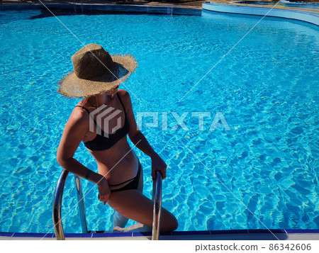 Portrait of a beautiful woman getting out of a swimming pool. beautiful blond hair tanned female model posing by blue pool water. Outdoor summer portrait of sexy girl in straw hat an sunglasses. Portrait of a beautiful woman getting out of a swimming pool. beautiful blond hair tanned female model posing by blue pool water. Outdoor summer portrait of sexy girl in straw hat an sunglasses. 86342606