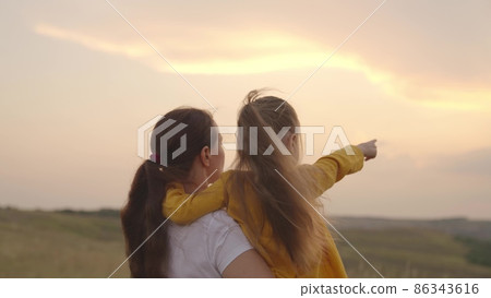 child with mother hugging at sunset, children shows mom by hand at sunset, childhood dream, happy family, love to travel together with family, kid and parent in nature sun, little daughter mom arms 86343616