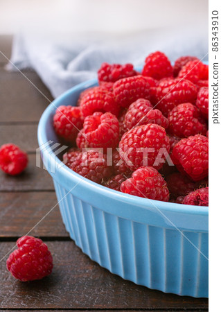 Red raspberry berry in plate on wooden table. 86343910