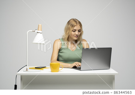 Portrait of a pretty young woman studying while sitting at the table with grey laptop computer, notebook. Portrait of a pretty young woman studying while sitting at the table with grey laptop computer, notebook. 86344563