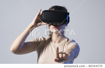 Close up of young woman stands in studio wearing VR glasses and swiping scrolling with hands in air. Virtual reality technology. 86344570