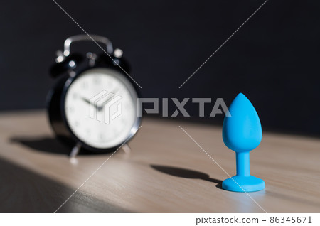 Blue latex anal plug and alarm clock on a wooden table. The time of carnal pleasures. Blue latex anal plug and alarm clock on a wooden table. The time of carnal pleasures. 86345671