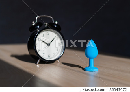 Blue latex anal plug and alarm clock on a wooden table. The time of carnal pleasures. 86345672