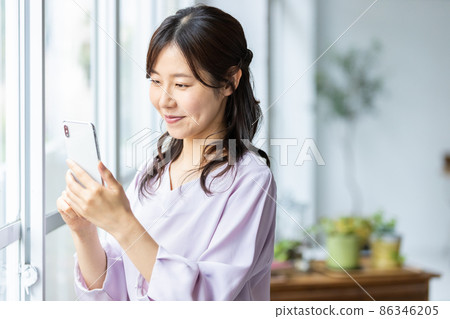 A smiling woman operating a smartphone in the room A smiling woman operating a smartphone in the room 86346205