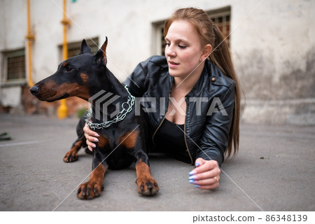 A girl in leather, with a Doberman, in an old yard. A girl in leather, with a Doberman, in an old yard. 86348139