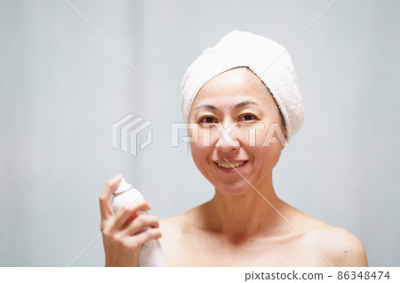 一個真臉的中年婦女，她用毛巾包住頭，在脖子和臉上蒙上霧氣。 86348474