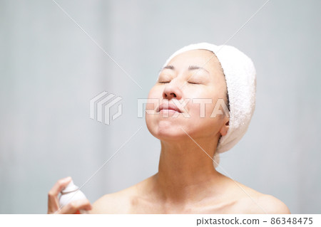 一個真臉的中年婦女，她用毛巾包住頭，在脖子和臉上蒙上霧氣。 86348475