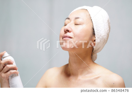 一個真臉的中年婦女，她用毛巾包住頭，在脖子和臉上蒙上霧氣。 86348476