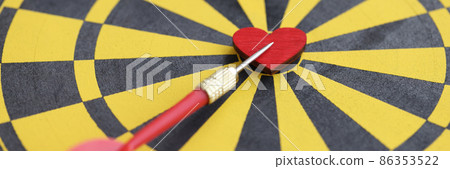 Red small wooden heart in center of dart board and dart closeup 86353522