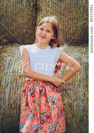 A schoolgirl with long flowing hair sits smiling on a log in a pink dress A schoolgirl with long flowing hair sits smiling on a log in a pink dress 86353991