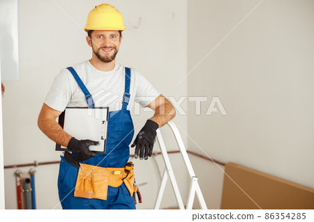 Smiling repairman holding clipboard and smiling at camera while standing in new apartment 86354285