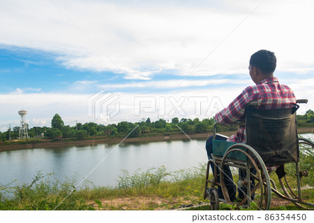 Young disabled man with river background.He is sitting on wheelchair Young disabled man with river background.He is sitting on wheelchair 86354450