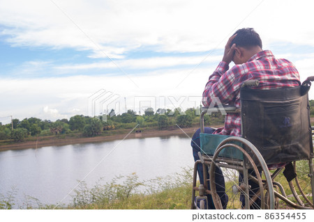 Young disabled man with river background.He is sitting on wheelchair Young disabled man with river background.He is sitting on wheelchair 86354455