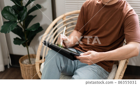 Technology Concept The young man who is sitting on the chair holding his iPad and noting something on it Technology Concept The young man who is sitting on the chair holding his iPad and noting something on it 86355031