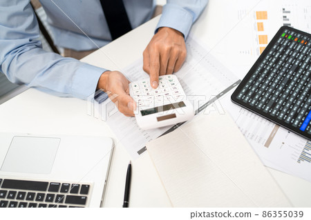 Working Man Conept The male officer sitting at his desk, holding the calculator, and pressing it Working Man Conept The male officer sitting at his desk, holding the calculator, and pressing it 86355039