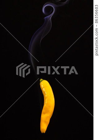 Yellow hot Mexican chili peppers against a black background with smoke coming from it, depicting it 86356683