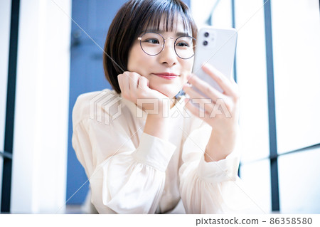 A woman with glasses lying on the floor and using a smartphone A woman with glasses lying on the floor and using a smartphone 86358580