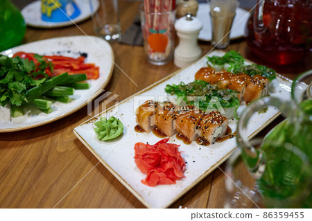White uramaki sushi tacoma maki sea food on a plate with salmon, avocado, ginger, soy sauce and wasabi on the table top with chopsticks. White uramaki sushi tacoma maki sea food on a plate with salmon, avocado, ginger, soy sauce and wasabi on the table top with chopsticks. 86359455