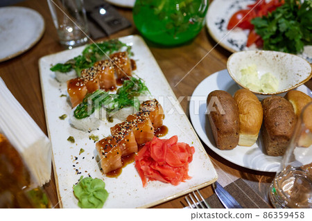 White uramaki sushi tacoma maki sea food on a plate with salmon, avocado, ginger, soy sauce and wasabi on the table top with chopsticks. White uramaki sushi tacoma maki sea food on a plate with salmon, avocado, ginger, soy sauce and wasabi on the table top with chopsticks. 86359458