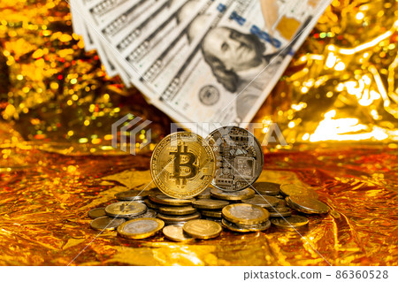 Two bitcoins on a stack of coins against a background of hundred-dollar bills arranged in a fan on a golden background. Two bitcoins on a stack of coins against a background of hundred-dollar bills arranged in a fan on a golden background. 86360528