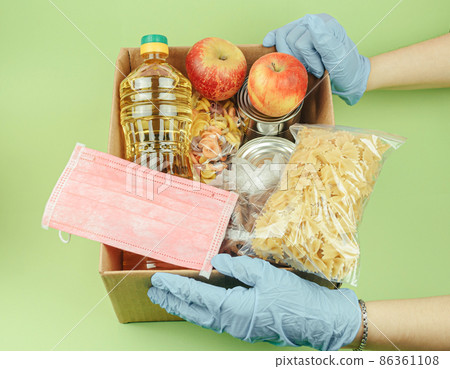 Volunteer in protective gloves with a donation of food boxes on a green background. Food delivery and virus protection. Donation and mercy concept. 86361108