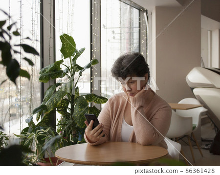 A brooding middle-aged woman with a smartphone in her hands in a cafe at a table. Dating on the Internet. Apps for seniors 86361428