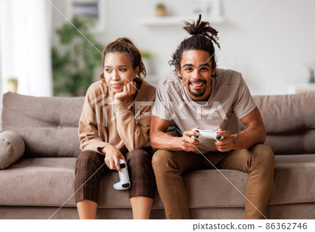 Boring date. Excited african american man playing video game and ignoring bored woman sitting beside Boring date. Excited african american man playing video game and ignoring bored woman sitting beside 86362746