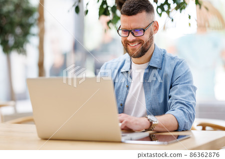 Happy young male businessman sitting in front of laptop outside working and having video conferencing online Happy young male businessman sitting in front of laptop outside working and having video conferencing online 86362876