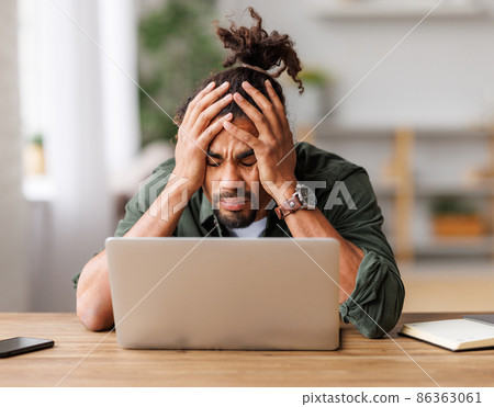 Frustrated young african american with eyes closed suffering from headache feeling stressed with work at laptop Frustrated young african american with eyes closed suffering from headache feeling stressed with work at laptop 86363061