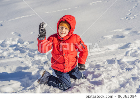 Funny little boy in blue winter clothes walks during a snowfall. Outdoors winter activities for kids. Cute child wearing a warm hat low over his eyes catching snowflakes with his tongue 86363084