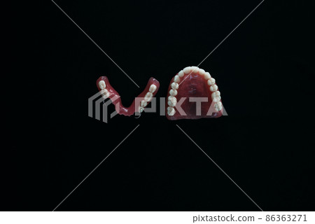 Full removable plastic denture of the jaws. A set of dentures on a black background. Two acrylic dentures. Upper and lower jaws with fake teeth. Dentures or false teeth, close-up. Copy space Full removable plastic denture of the jaws. A set of dentures on a black background. Two acrylic dentures. Upper and lower jaws with fake teeth. Dentures or false teeth, close-up. Copy space 86363271