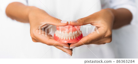 The dentist is holding dentures in his hands. Dental prosthesis in the hands of the doctor close-up. Front view of complete denture. Dentistry conceptual photo. Prosthetic dentistry. False teeth 86363284