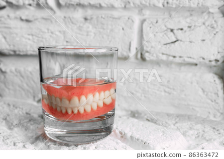 A denture in a glass of water. Dental prosthesis care. Full removable plastic denture of the jaws. Two acrylic dentures. Upper and lower jaws with fake teeth. Dentures or false teeth, close-up. A denture in a glass of water. Dental prosthesis care. Full removable plastic denture of the jaws. Two acrylic dentures. Upper and lower jaws with fake teeth. Dentures or false teeth, close-up. 86363472