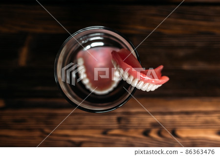 A denture in a glass of water. Dental prosthesis care. Full removable plastic denture of the jaws. Two acrylic dentures. Upper and lower jaws with fake teeth. Dentures or false teeth, close-up. A denture in a glass of water. Dental prosthesis care. Full removable plastic denture of the jaws. Two acrylic dentures. Upper and lower jaws with fake teeth. Dentures or false teeth, close-up. 86363476